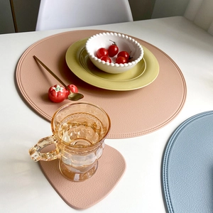 Pink round PU leather placemat and coaster set with textured lychee grain on white table