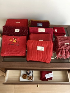 Detalle de bufandas de punto rojas y beige con bordado de oso apiladas en estante de madera