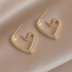 Close-up of golden heart earrings with zircon studs on soft beige silk background