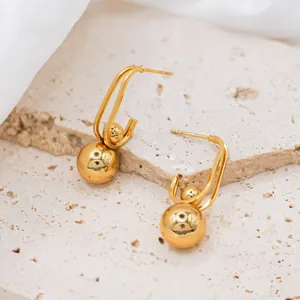 Detailed view of U-shaped gold earrings with polished sphere drops on a stone background
