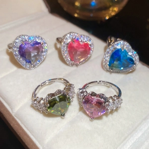 Close-up of five heart-shaped zircon rings in various colors inside a velvet jewelry box