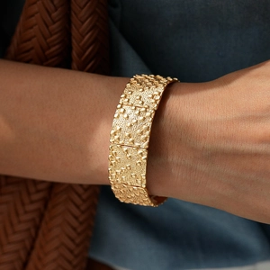 Gros plan d'un large bracelet doré avec des motifs métalliques carrés en relief