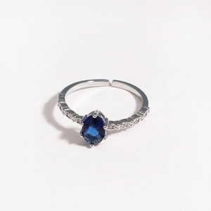 Detailed close-up of oval blue zircon silver ring with small diamond accents on white base