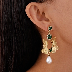Detail of vintage gold butterfly earrings with green stones and white teardrop pearl on model