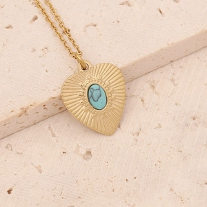 Vintage gold heart necklace with turquoise stone inlay on minimalist beige stone