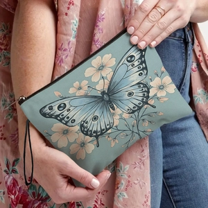 Floral butterfly print makeup bag with zipper and wrist strap held by a model