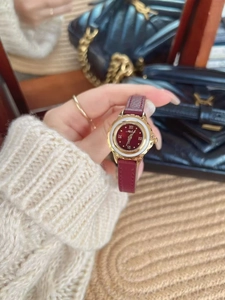 Detailed view of women's vintage red leather watch with golden clover case and roman numerals
