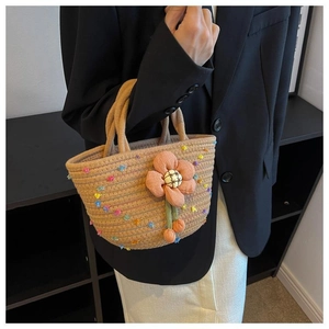 Detail of hand-woven beige rope tote bag with colorful pom-poms and 3D floral accent