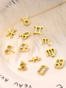 Flat lay of 12 gold zodiac charms for DIY jewelry on a white feather and plate