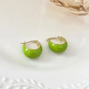 Elegant avocado green enamel C-shaped hoop earrings with gold plating on a ceramic tray