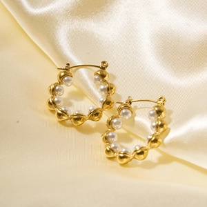 Close-up of gold hollow hoop earrings with white pearls on elegant cream satin fabric