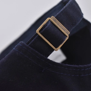 Detalle de gorra de algodón azul marino con hebilla de bronce ajustable y costuras