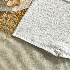 Close-up of white textured ruched fabric of a swimsuit on a beige striped background