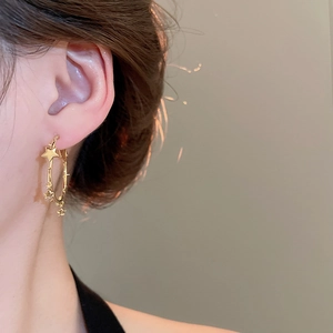 Close-up of model wearing gold star-accented hoop earrings with metallic finish