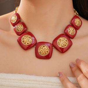 Primo piano di una collana vintage in smalto rosso con motivi dorati su modella.