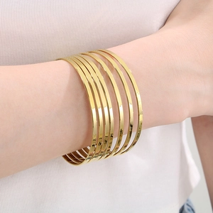 Detail of seven stacked 18k gold polished stainless steel bangles worn on a wrist