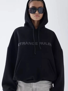 Detail of oversized black hoodie with kangaroo pocket and ETRANGE RULE printed chest