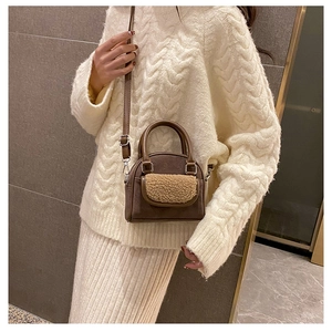 Detail of a brown leather shoulder bag with beige plush trim held by a model