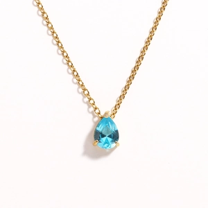 Detail of gold chain necklace featuring a teardrop blue zircon stone in 4-prong setting