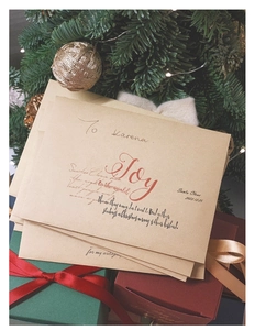 Festive Kraft paper envelope with artistic 'Joy' lettering among Christmas decorations