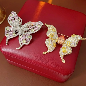 Detailed macro of gold-plated butterfly brooches with colorful cubic zirconia on red velvet
