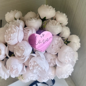 Gros plan d'un topper de gâteau cœur rose parmi un bouquet de fleurs de soie blanches