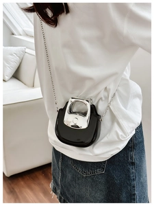 Detail of a mini black glossy shoulder bag with a silver handle and metal chain strap
