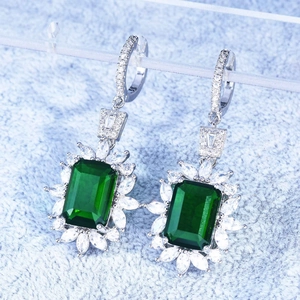 Detail of emerald green square cut earrings with white stone petals on a display stand