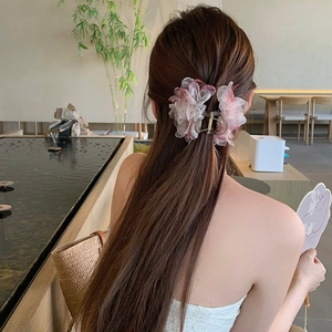 Dettaglio di una pinza per capelli con fiore in organza sfumata rosa e bianca su uno chignon