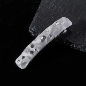 Macro shot of silver rhinestone hairpin with irregular hammer texture on dark stone surface