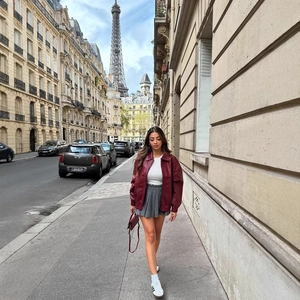 Women's burgundy woven faux leather bomber jacket paired with grey pleated skirt