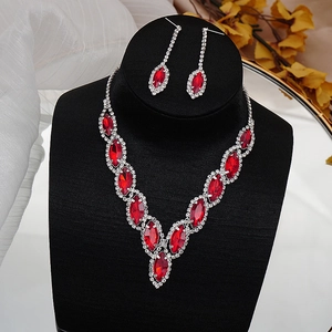 Detailed view of elegant silver necklace and red crystal earrings set on a black display