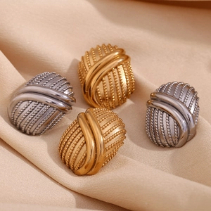 Dettaglio di orecchini vintage ovali in oro e argento su elegante seta champagne