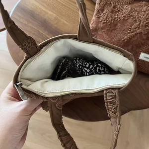 Top view of brown suede handbag featuring floral embroidery and internal zipper pocket