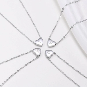 Close-up of four silver heart necklaces featuring engraved Y, S, M, Q letters on white silk