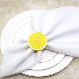 Detailed view of a bright yellow lemon slice napkin ring on a white folded napkin