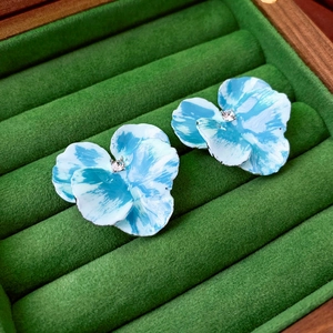 Close-up of blue iris enamel flower earrings with central crystal on green velvet
