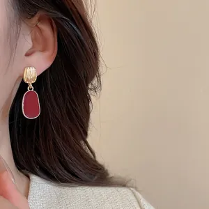 Macro shot of elegant red oval earrings with textured gold finish worn by a model