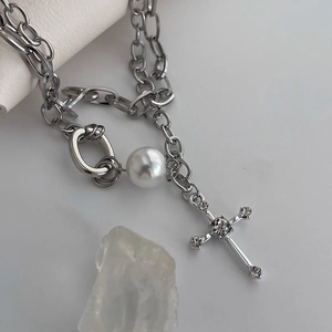Detailed view of silver cross pendant with rhinestones and white pearl on a double chain