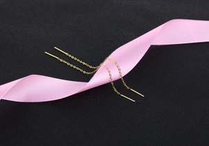 Macro shot of gold tassel drop earrings with long O-chain on silk ribbon and black background