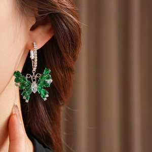 Close-up of a silver butterfly earring with green and white zircons worn by a model