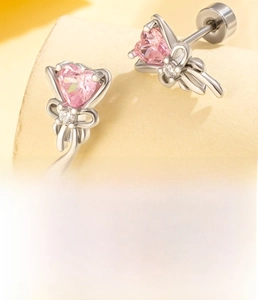 Macro shot of silver bow heart earrings with pink zircon on beige curved pedestal