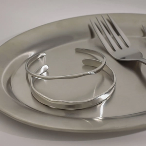 Set of two silver wavy stainless steel bracelets displayed on a metallic tray