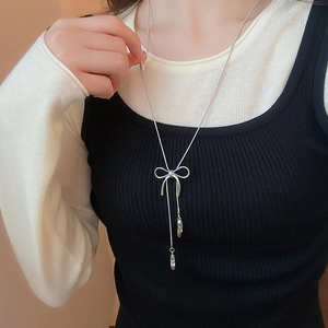 Detail of silver bow and ballet slipper pendant on a long chain worn by model