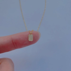 Detail of a mini gold-plated square pendant with pavé cubic zirconia held on a fingertip