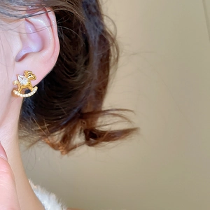 Close-up of golden rocking horse earring with sparkling cubic zirconia on model
