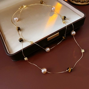 Detail of layered necklace featuring pink pearls, tiger eye beads and gold hollow spheres