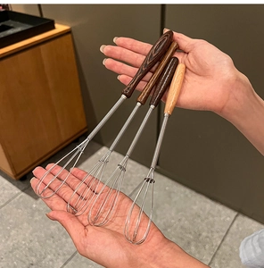 Detail view of four stainless steel whisks with varied wooden handles for home baking
