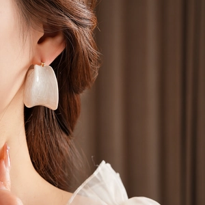 Close-up of a white marble texture acrylic earring with gold metal pin on a female model