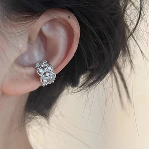 Close-up of a silver hollow-out zircon cross ear cuff worn on the ear cartilage